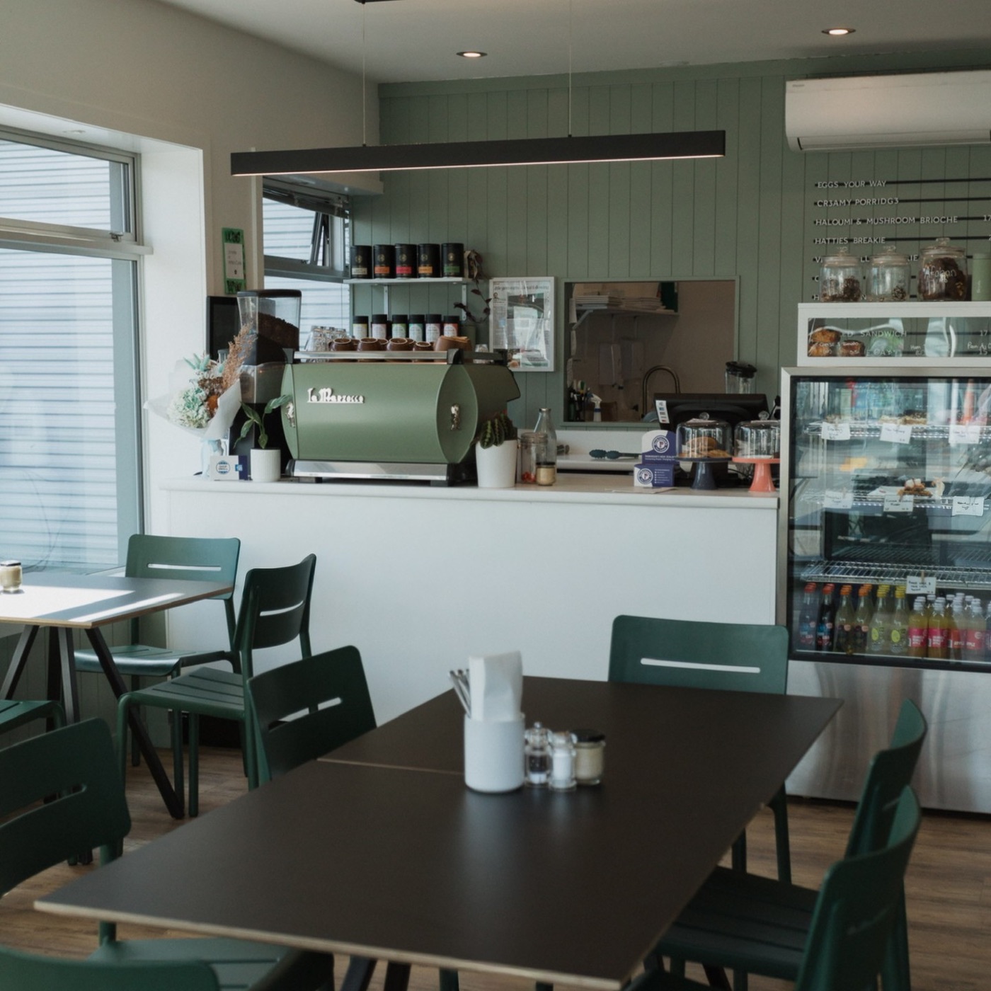 The cafe inside: sage green panelling, a dark green espresso machine on the counter and green chairs at dark tables