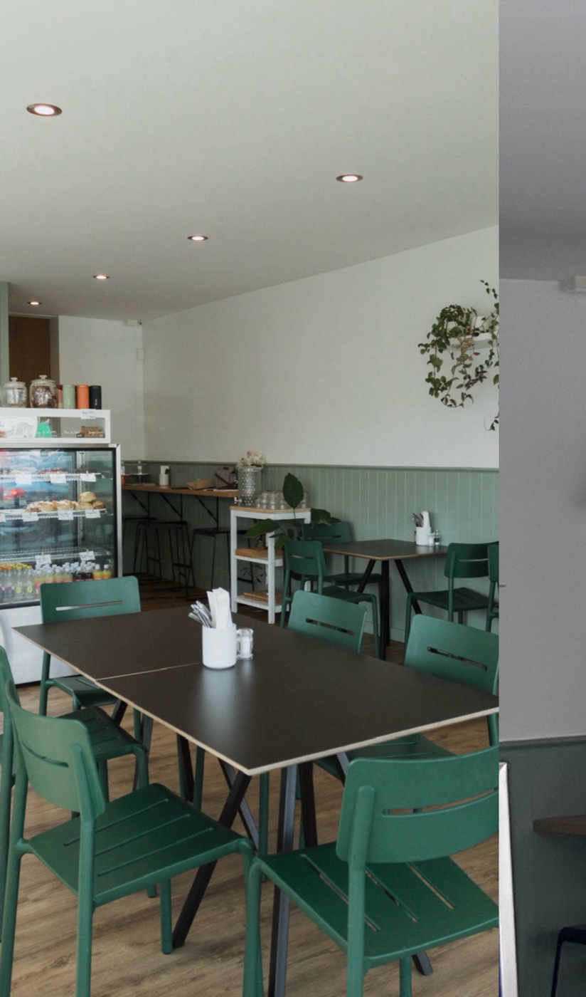 Dark tables and green chairs in a bright room with a pale green panelled wall and the cabinet at the back
